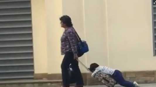 La madre lleva a su hijo arrastrando a la escuela sobre una mochila